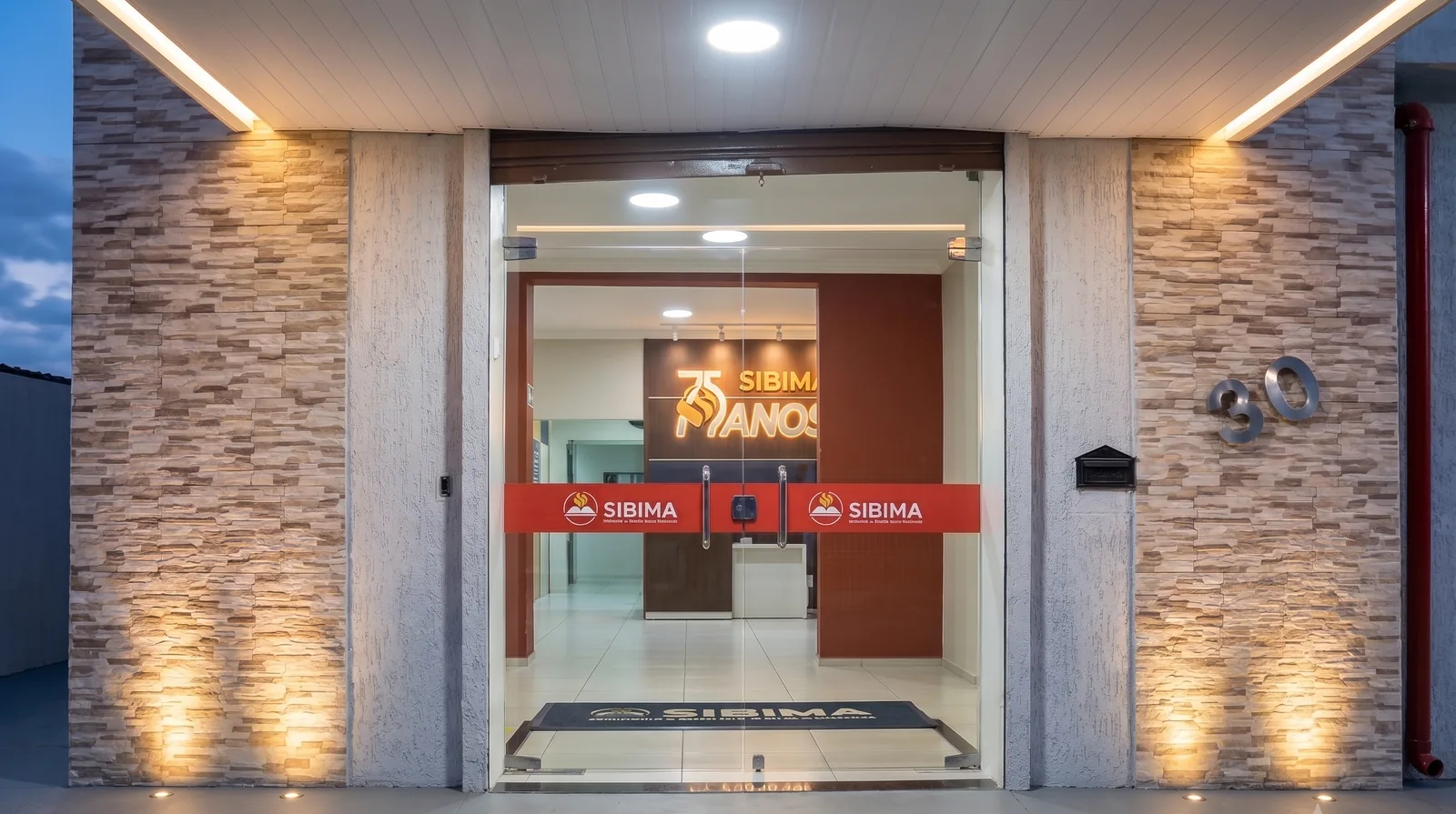 Entrada do SIBIMA, com as portas de vidro iluminadas e o tapete com o nome do seminário